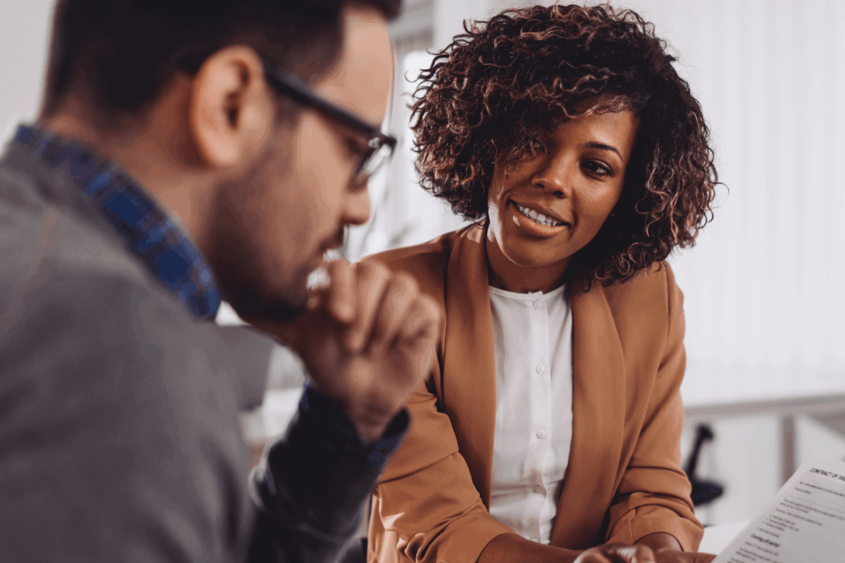A man and a women sitting on a desk talking.